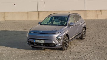 Hyundai Kona Elektro fotografiert in der Abendsonne schraeg von vorn vor einem neutralen Gebbäude