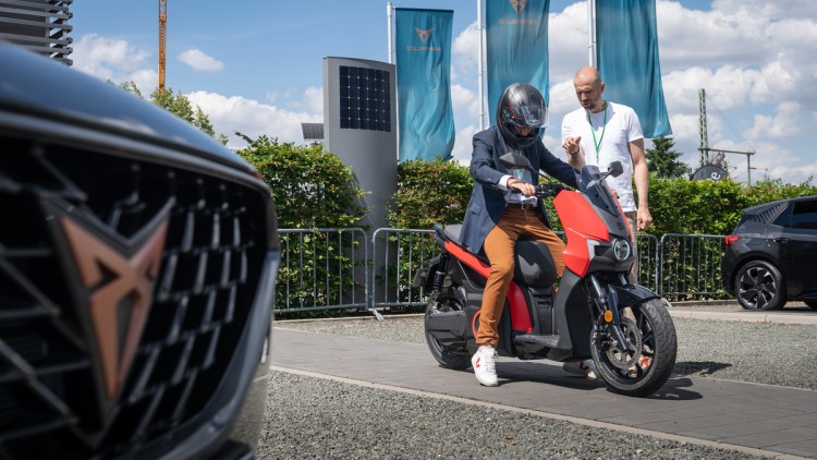 Seat Mó in rot vor Cupra-Fahnen auf Schotterplatz