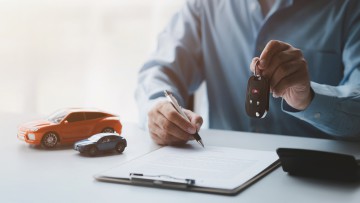 Autohändler unterschreibt Kaufvertrag und übergibt Fahrzeugschlüssel