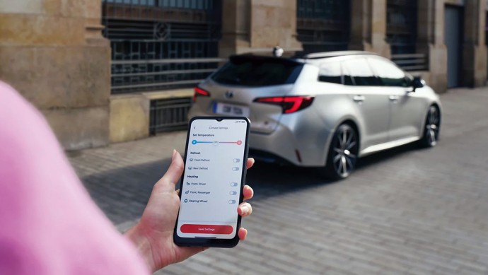 Kunde blickt auf Smartphone mit Toyota App, im Hintergrund steht ein Toyota