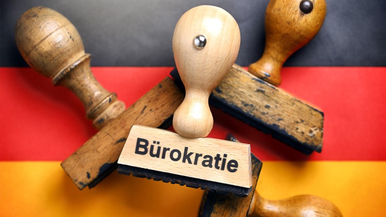 Stempel mit dem Auftruck Bürokratie sowie weitere Stempel liegen auf einer Deutschland-Fahne