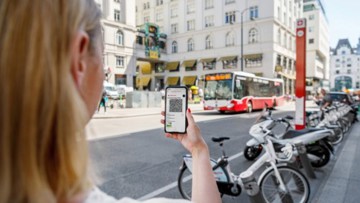 Frau mit Smartphone in Wien zur Einführung des digitalen Tickets bei den Wiener Linien - im Hintergrund ein Linienbus 
