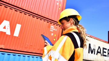 Frau mit Tablet vor Containerstapel