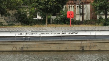 Binnenschiff mit Aufschrift "Captain Niveau, wir sinken"