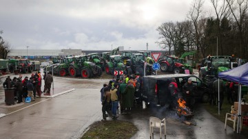 Landwirte stehen mit ihren Traktoren vor einem Zentrallager von Aldi. Seit Sonntagnacht (14. Januar)  blockieren Landwirte den Warenverkehr im Landkreis Harburg.