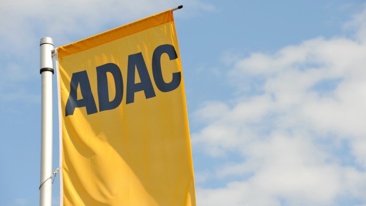 Eine glebe Fahne mit schwarzem ADAC-Logo vor blauem Himmel mit einigen weißen Wölkchen