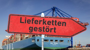 Ein rotes, zerkratztes Hinweisschild mit der Aufschrift "Lieferketten gestört" vor der MOL TRUST, einem der größten Containerschiffe der Welt, am HHLA Container Terminal Burchardkai im Hamburger Hafen