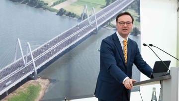 Staatssekretär Oliver Luksic im anzug vor Bild mit Autobahnbrücke