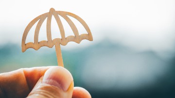 Ein Miniatur-Holz-Regenschirm stellt symbolisch einen Schutzschirm dar