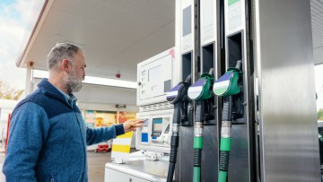 Ein Mann an der Tankstelle zahlt für den Tank seines Autos am Automaten neben der Zapfsäule