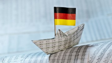 Papierschiff mit deutscher Flagge auf Zeitungsseiten mit Kurstabellen
