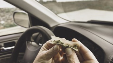 Hände eines Mannes, der Marihuana in einem Fahrzeug zu einem Joint dreht
