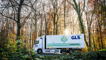 Der GLS Wasserstoff-Lkw fährt bei Sonnenschein im Herbst durch einen lichten Wald
