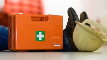 Person auf dem Boden nach Arbeitsunfall mit Verbandskasten