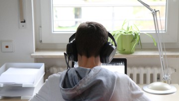 Eine junge Person arbeitet mit Laptop und Headset zuhause im Homeoffice.