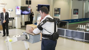 Bundesarbeitsminister Hubertus Heil testet am Fraunhofer IML ein Exoskelett und übergibt Paket an autonomen Roboter