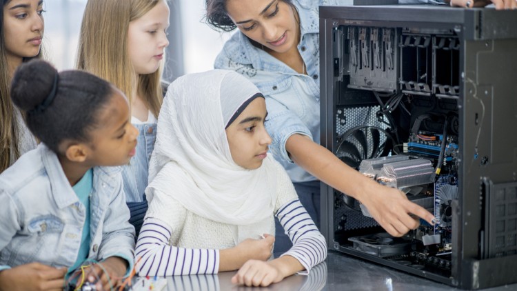 Eine Frau zeigt vier Mädchen das Innere eines Computers