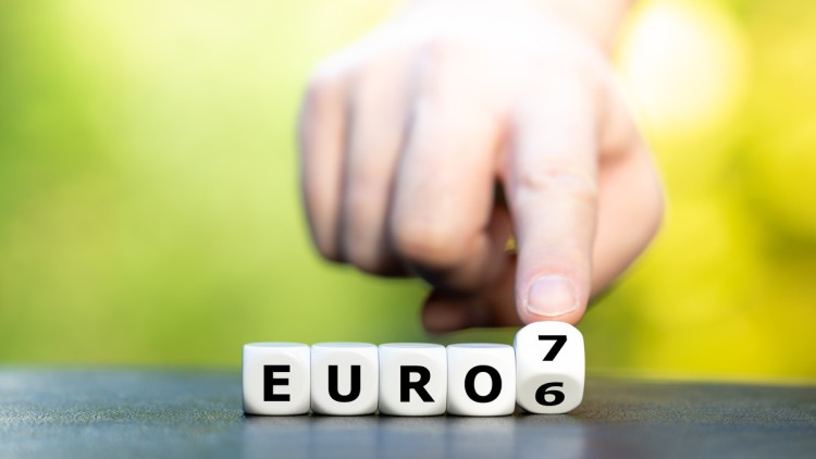 Symbol für die Änderung der Europäischen Emissionsverordnung von der Euro-6-Emissionsnorm zur Euro-7-Norm. Im Bild die Buchstaben für Euro und die Zahl 6 auf Würfeln, bei der ein Finger den Würfel grade vin 6 auf 7 dreht
