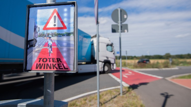 Ein LKW biegt am 23. Juli 2020 an einer Kreuzung rechts ab, während ein Schild mit Aufschrift „Toter Winkel“ eines Schutzsystems hell aufleuchtet und Fahrradfahrer warnt. Zwar schauen Lastwagenfahrer beim Abbiegen in den Spiegel, die Fahrradfahrer im tote